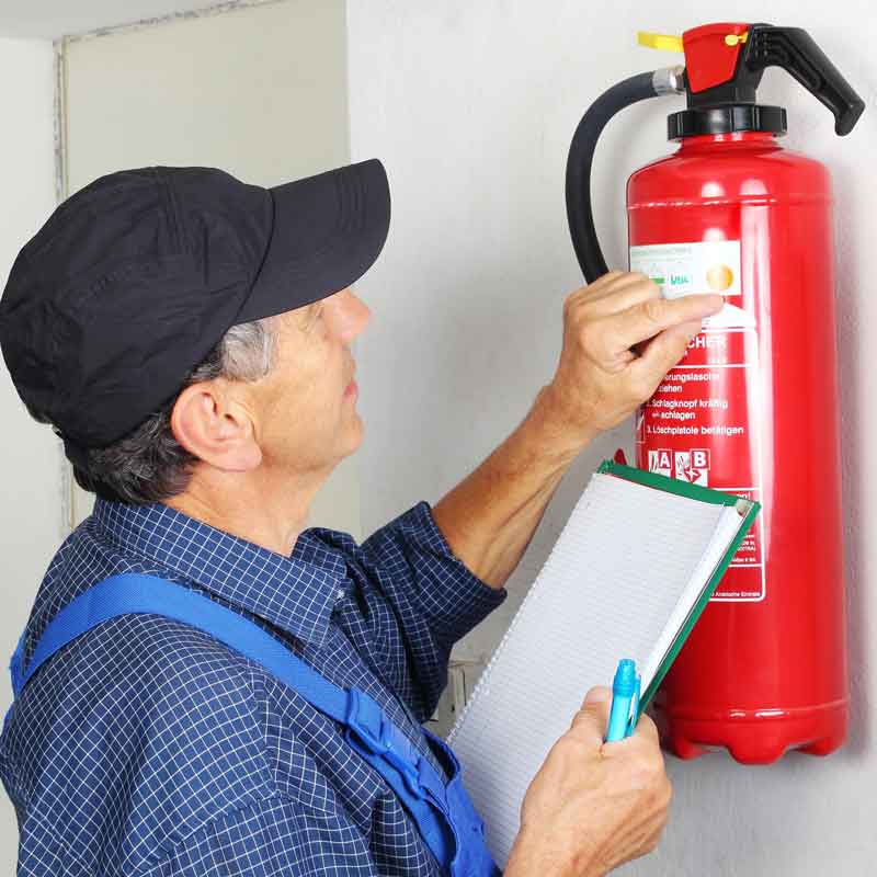 Mann in Blauer Arbeitshose zeigt auf Feuerlöscher_Brandschutz Muenchen_Huber-Trockenbau-Muenchen